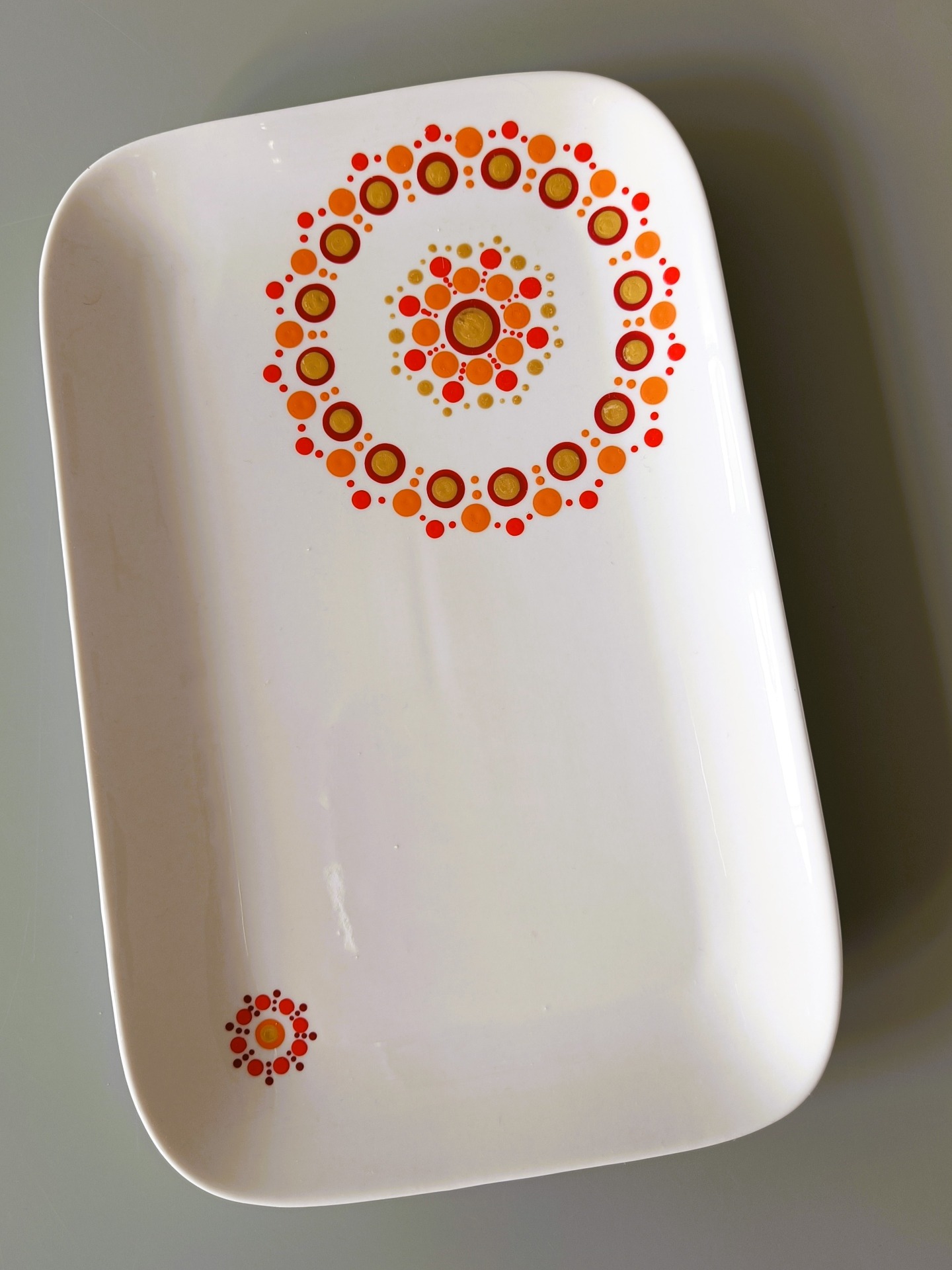 Witte serveerschaal met decoratieve cirkel van rode en oranje stippen en gouden schijfjes in het midden.